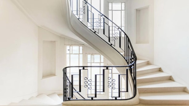 Una escalera en espiral con barandilla de metal negro en un espacio interior luminoso y blanco.