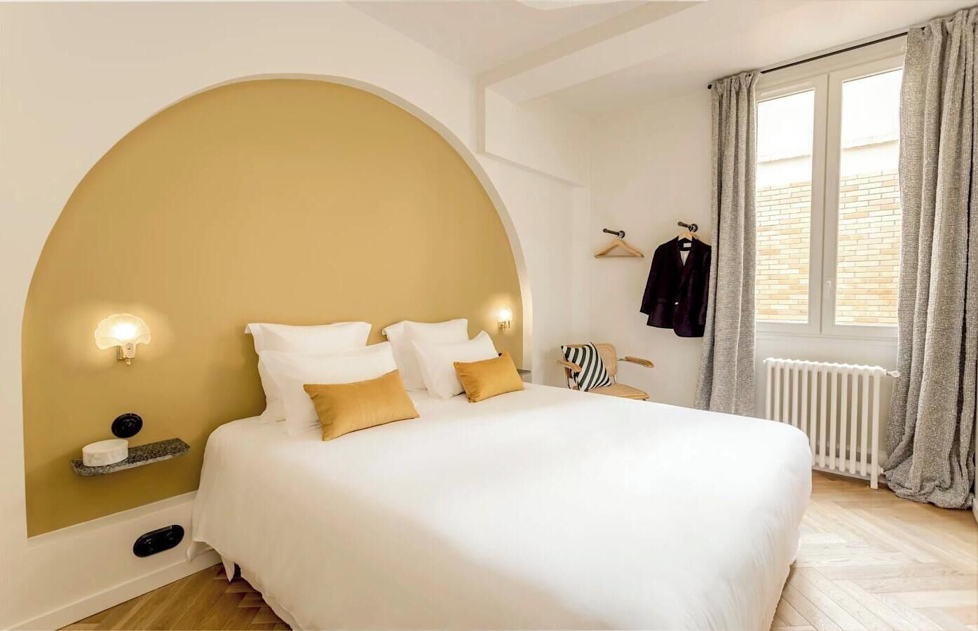 A bedroom with a large bed, a curved wall, a radiator, and a window with curtains.