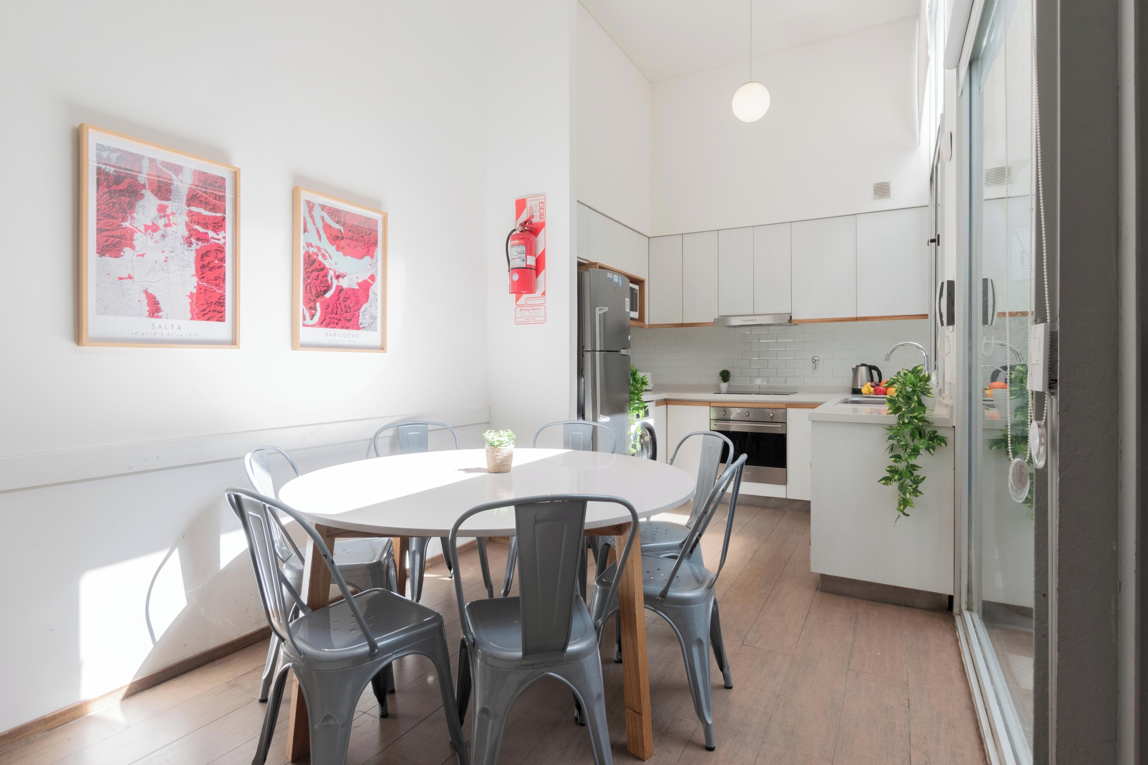 Une cuisine moderne avec des meubles blancs, un réfrigérateur en acier inoxydable et un coin repas comprenant une table ronde et des chaises grises.