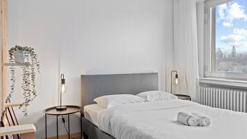 A modern bedroom with a bed, bedside lamps, a window with a view, and a plant on a shelf.