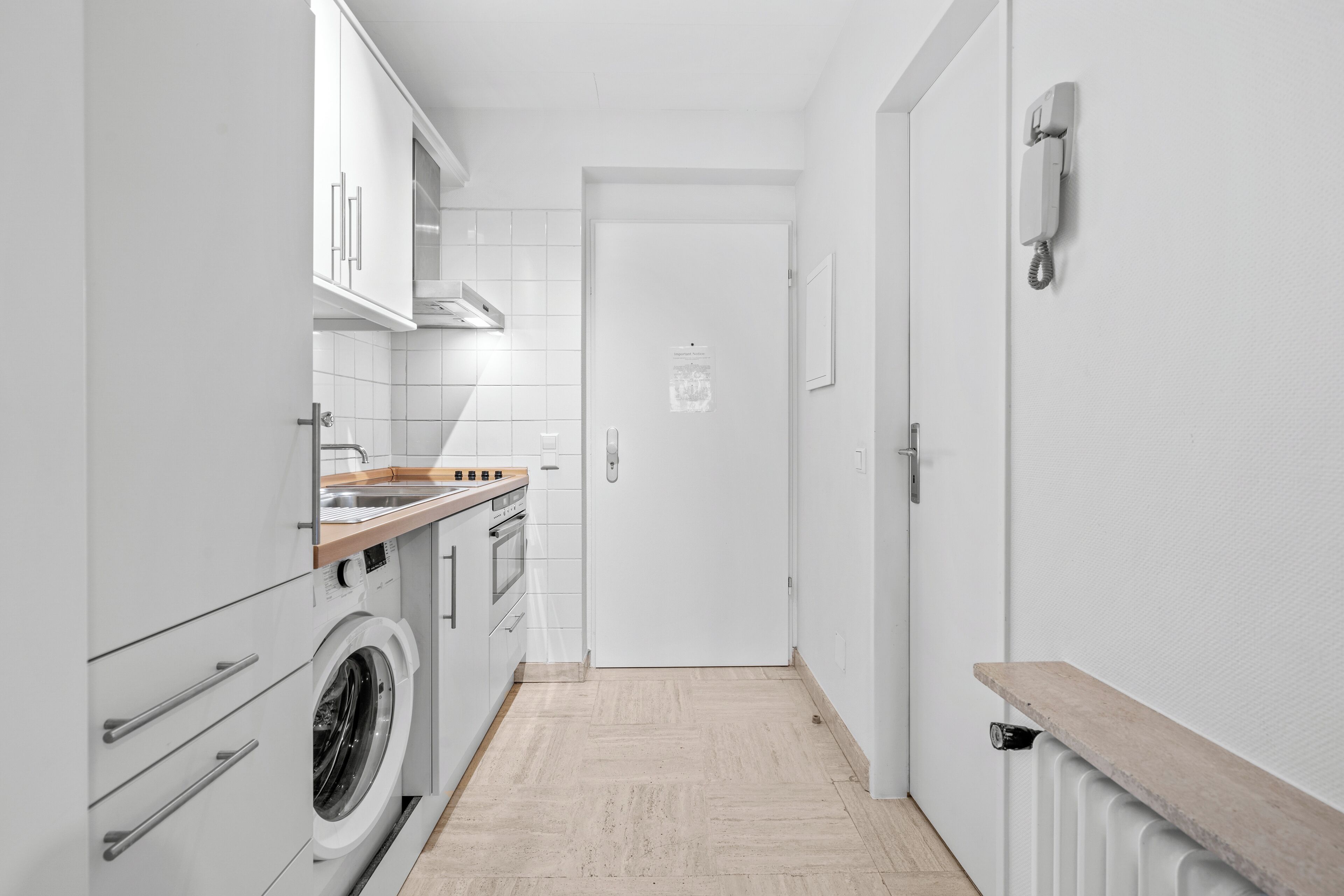 Eine schmale Küche mit weißen Schränken, einer Waschmaschine und einer Holz Arbeitsplatte.
