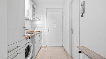 Eine schmale Küche mit weißen Schränken, einer Waschmaschine und einer Holz Arbeitsplatte.
