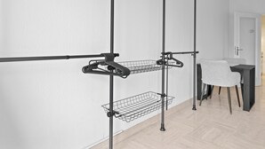 A modern room with a white wall, a black metal rack with wire baskets, a grey chair, and a small table.