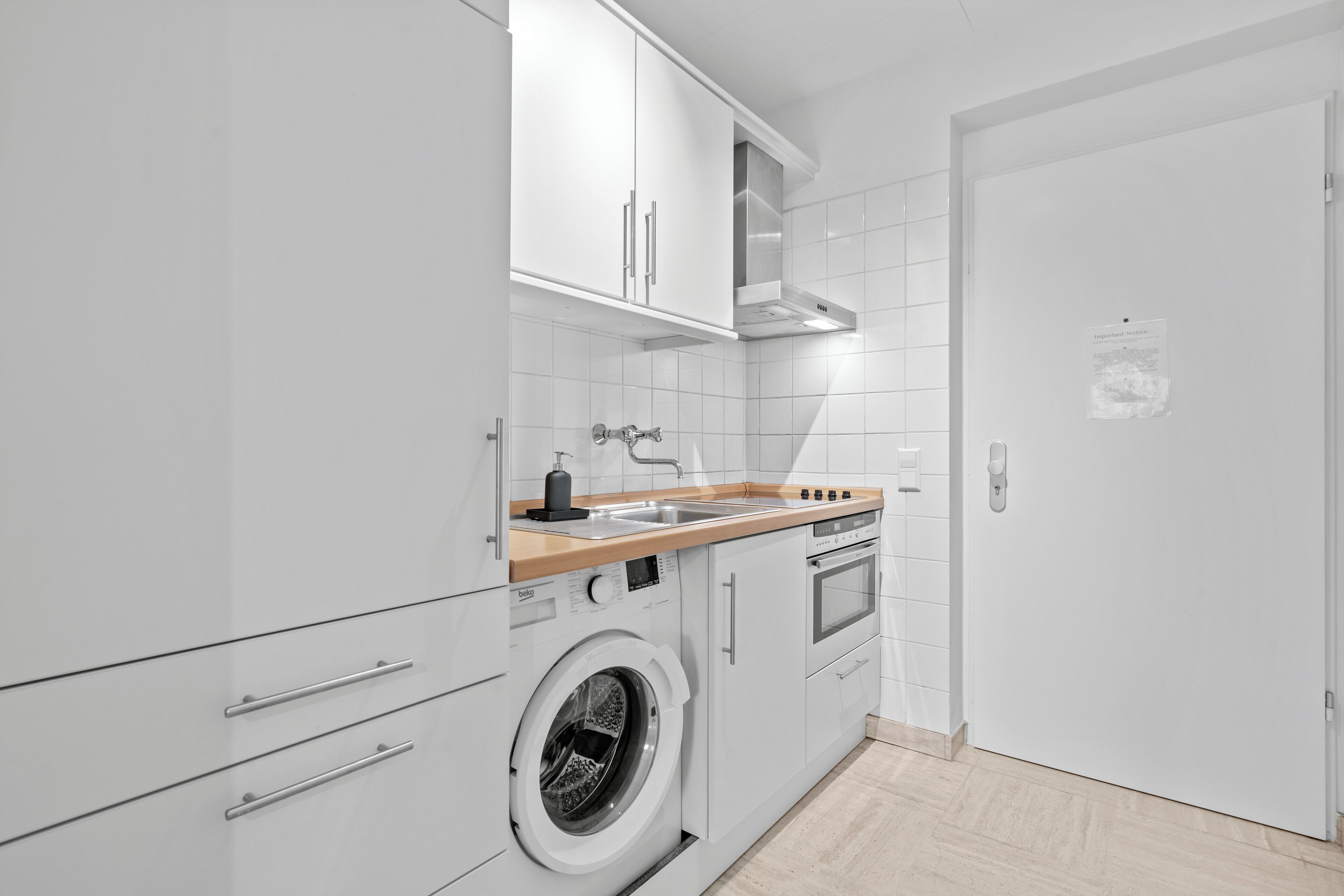 Una cocina moderna con armarios blancos, lavadora integrada, encimera de madera y campana extractora de acero inoxidable.