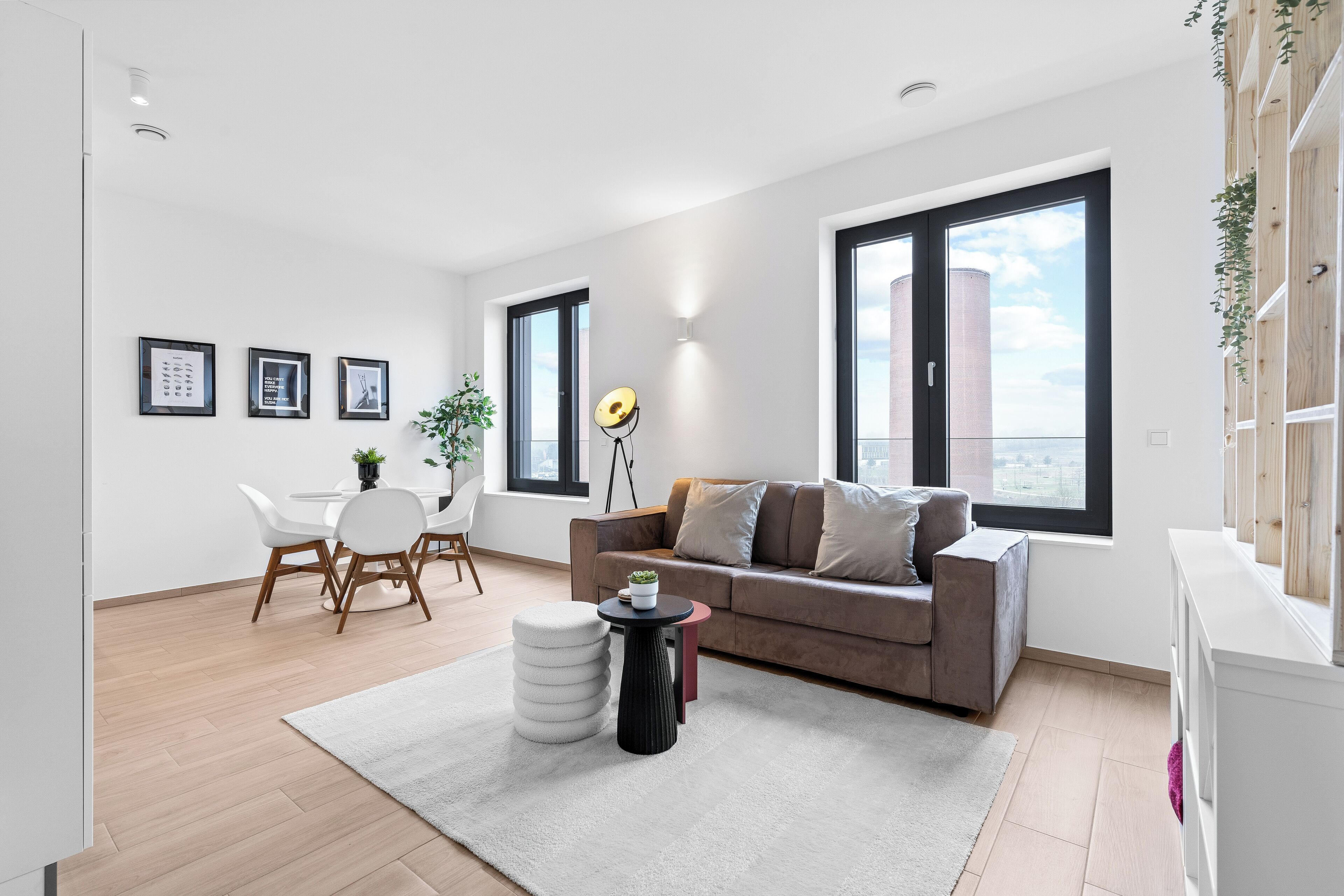 Ein modernes Wohnzimmer mit einer Couch, einem Esstisch und Stühlen. Große Fenster bieten Blick auf ein Gebäude.