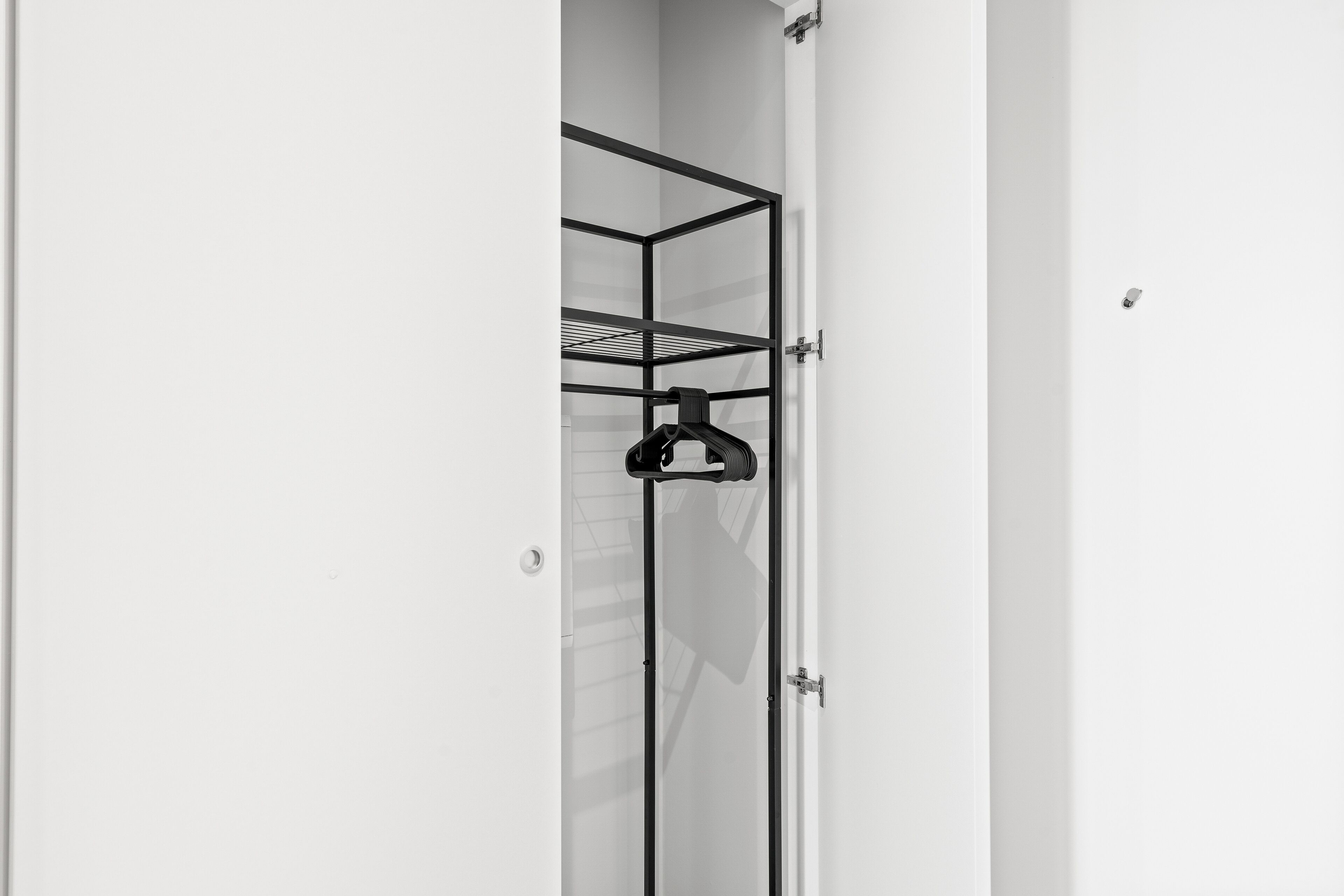 Um quarto branco com uma estante de metal preto na parede.