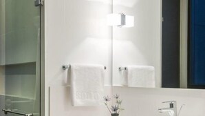 A modern bathroom with a glass shower enclosure, a white sink with a mirror above, and a wooden cabinet below. - Ochenta Diez by Wynwood House (Bogotá)