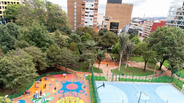 An outdoor playground with colorful play areas and basketball courts surrounded by trees and buildings. - Ochenta Diez by Wynwood House (Bogotá)