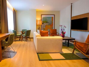 Una habitación de hotel moderna con sofá, sillas, una mesa de comedor y televisión.