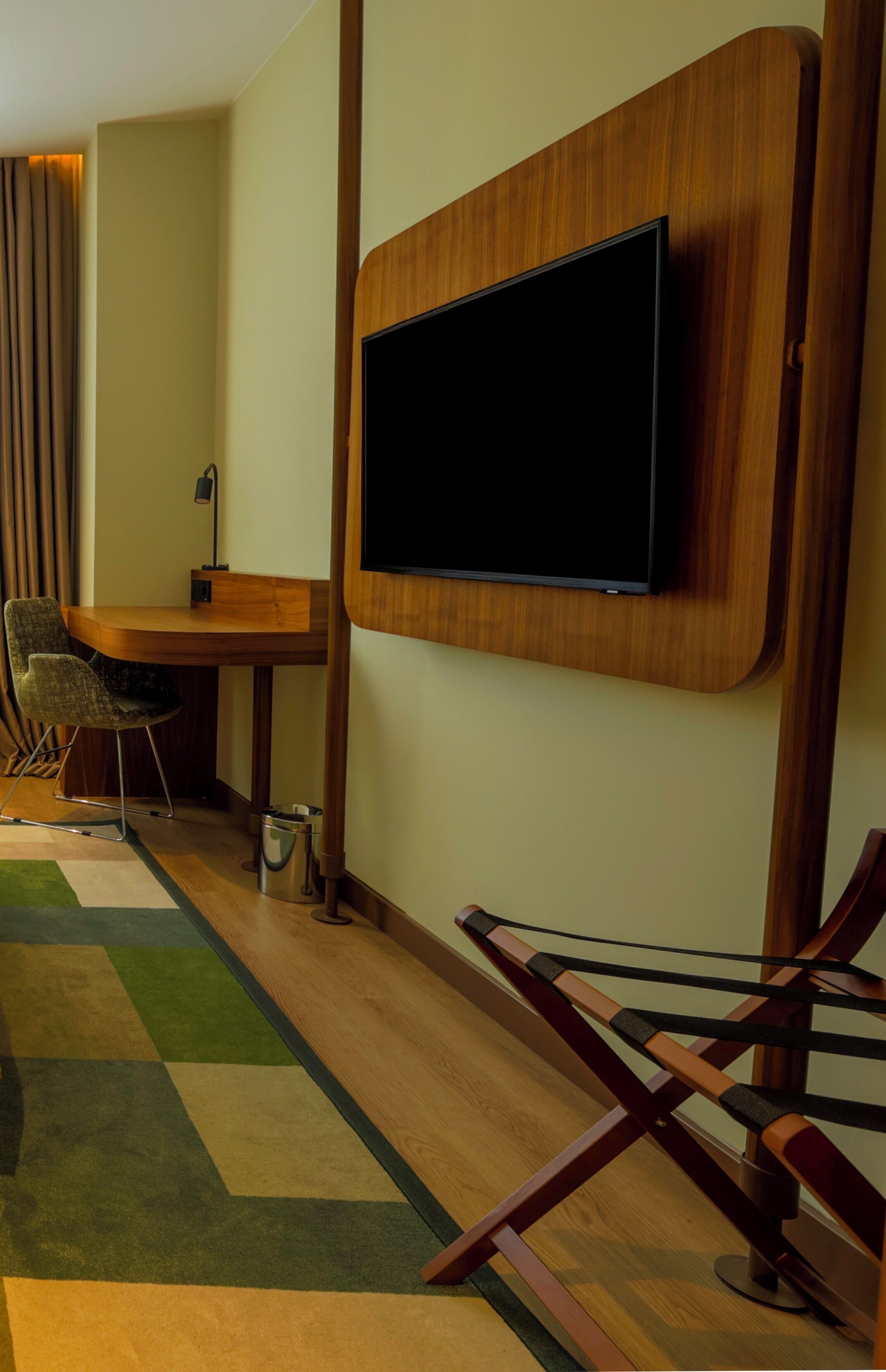 Ein modernes Zimmer mit Flachbildfernseher an der Wand, einem Holztisch, einem Stuhl und einem farbenfrohen Teppich.