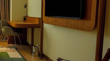 Ein modernes Zimmer mit Flachbildfernseher an der Wand, einem Holztisch, einem Stuhl und einem farbenfrohen Teppich.