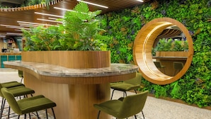 A reception area with a wooden counter, green upholstered chairs, a large mirror, and a green wall with plants. - ibis Styles Istanbul Kurtkoy (Istanbul)