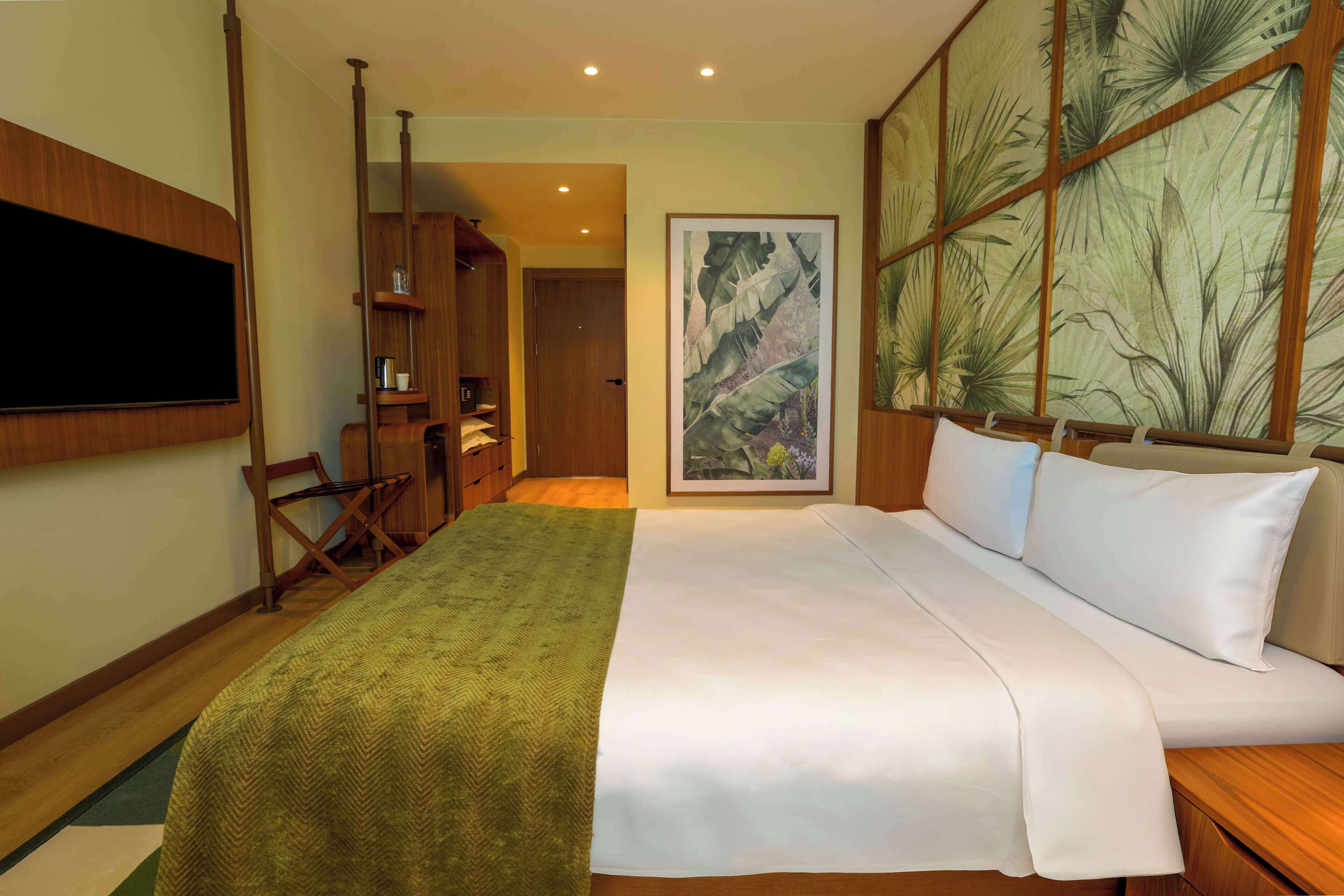 Habitación de hotel con una cama grande, muebles de madera, un televisor de pantalla plana y un mural temático tropical.