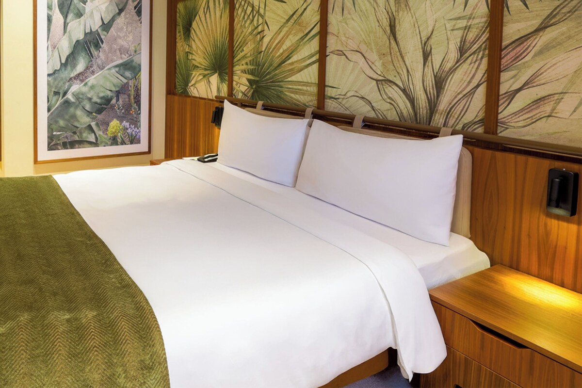 A hotel room with a large bed, a wooden headboard, and a wall-mounted artwork.
