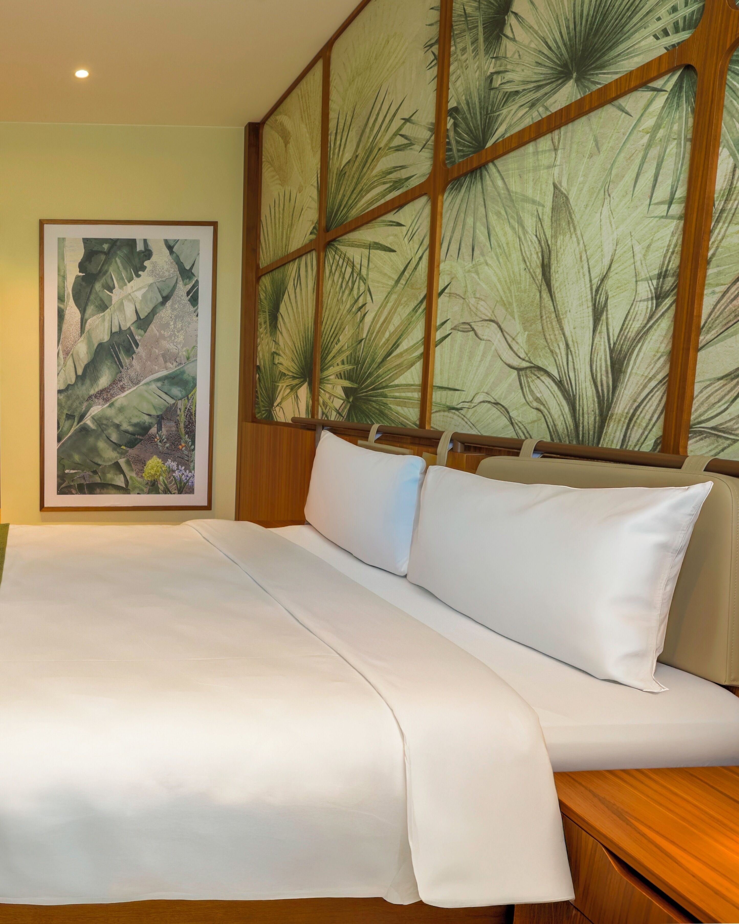 Camera d'albergo con un letto grande, una testiera in legno e una parete decorata a tema tropicale.