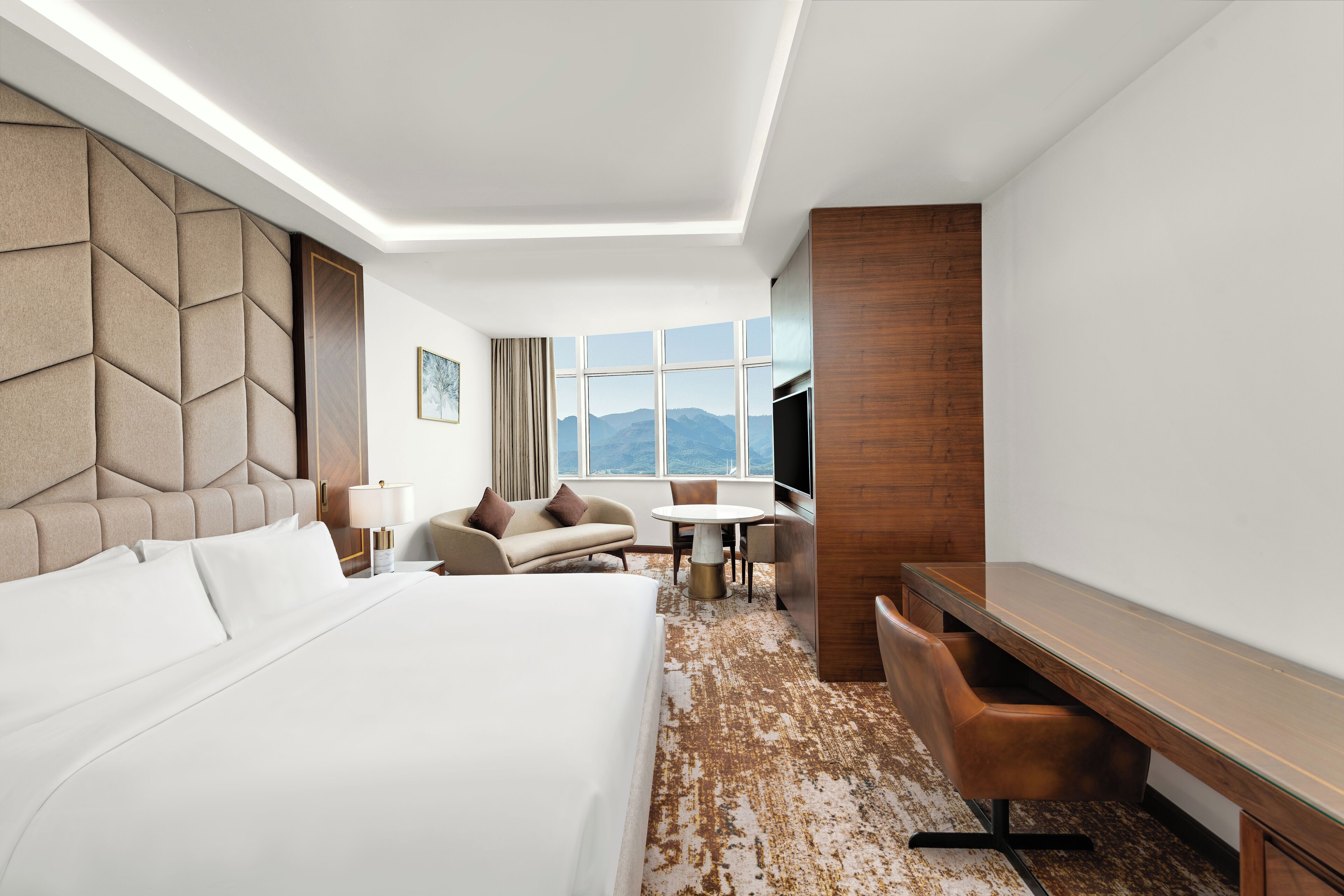 Habitación de hotel con una cama grande, un sofá, un escritorio y vistas a las montañas a través de la ventana.