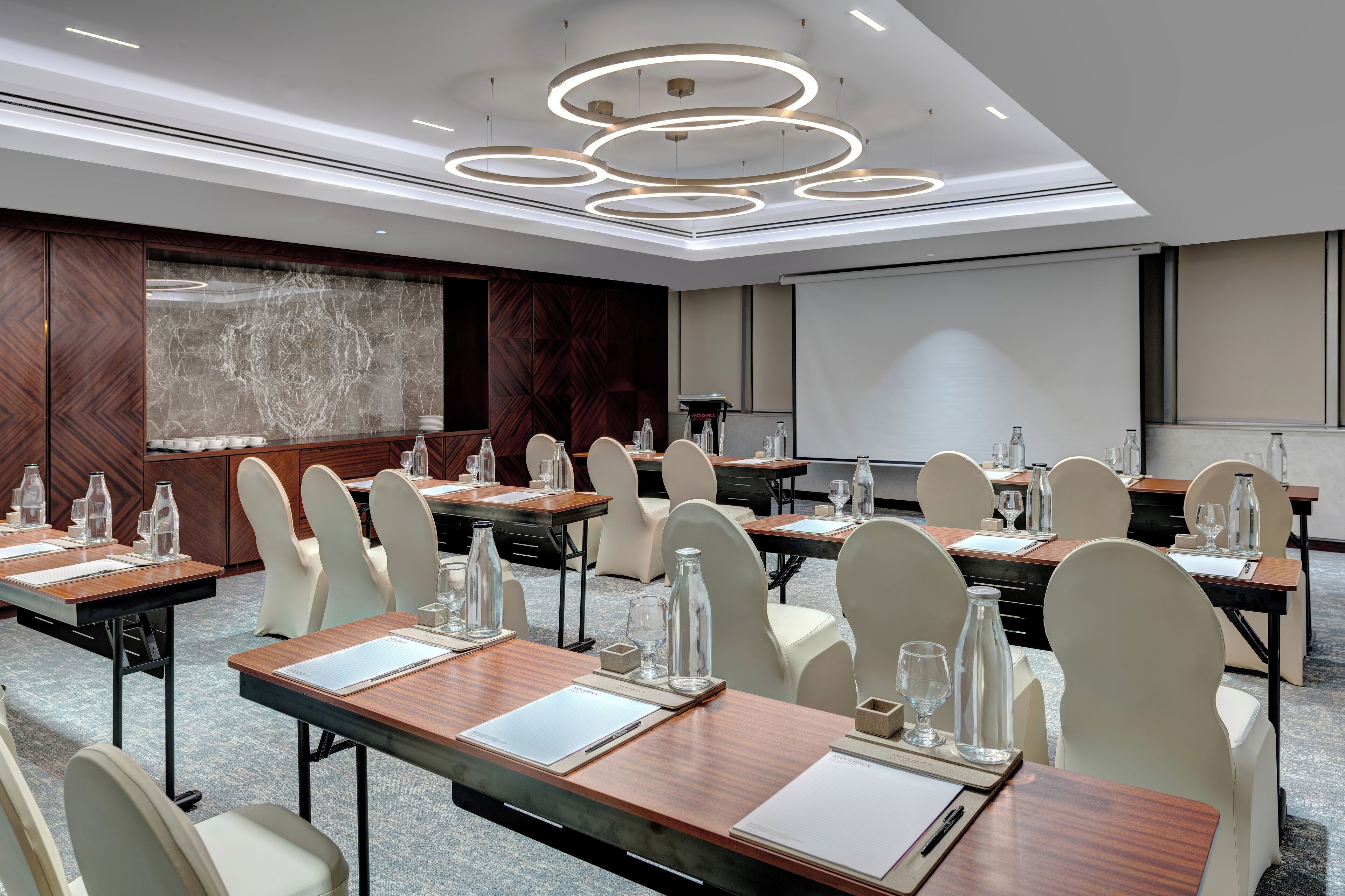 Un salón de conferencias con varias mesas, sillas y una pantalla grande.