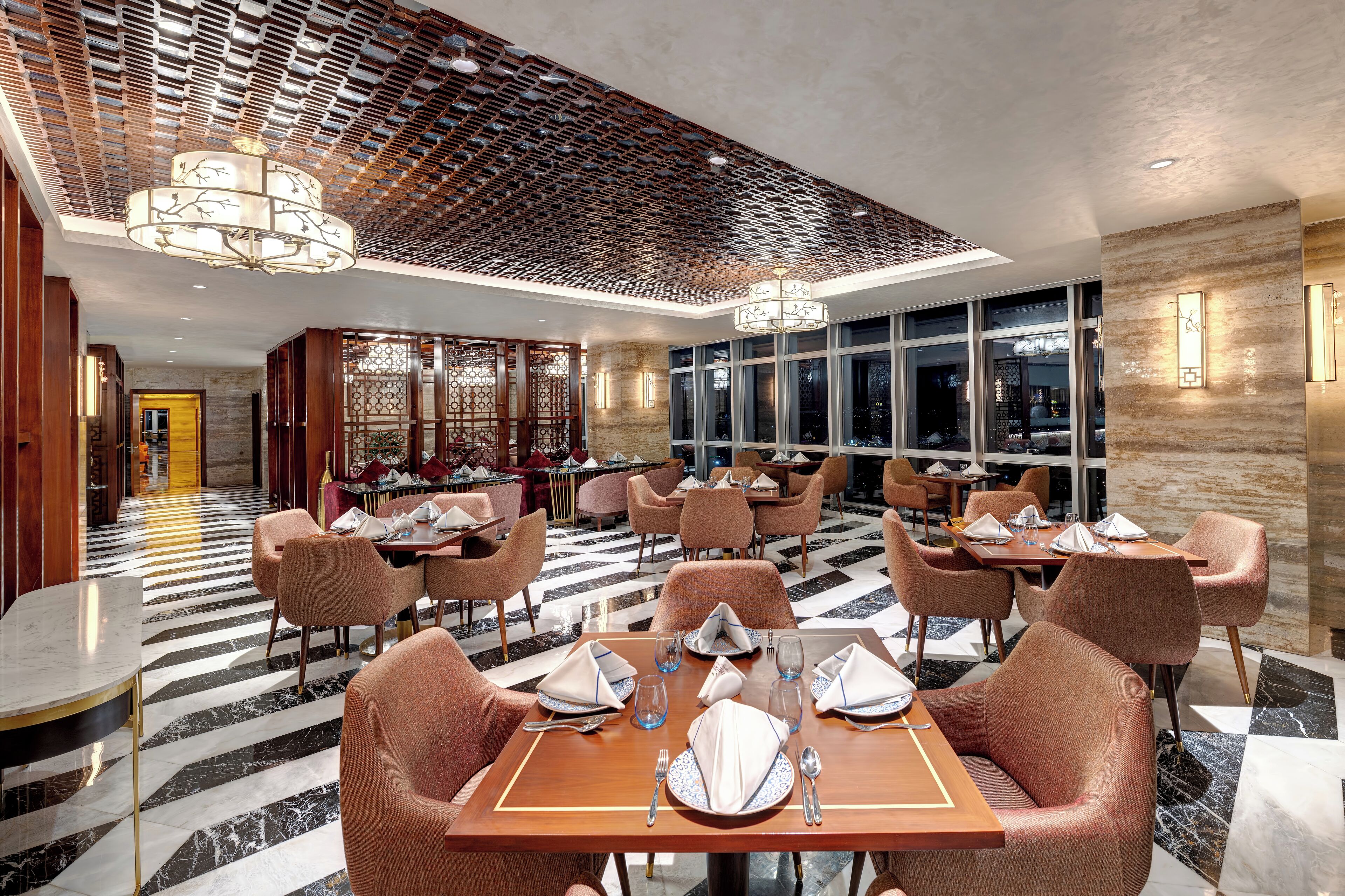 Un restaurante moderno con suelo a cuadros blanco y negro, techo de madera y mobiliario contemporáneo.