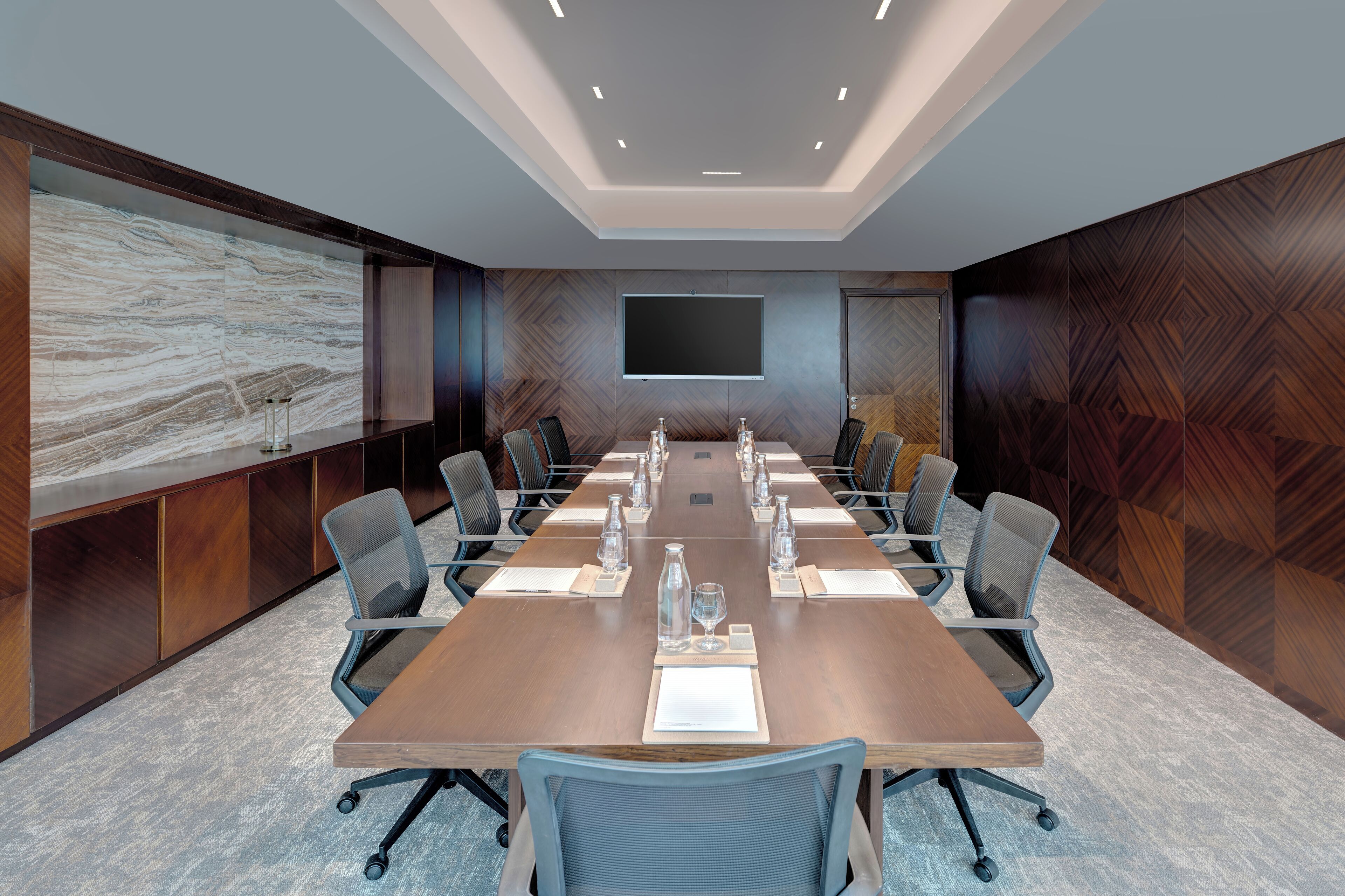 A conference room with a long table, multiple chairs, a large screen, and a wooden accent wall.