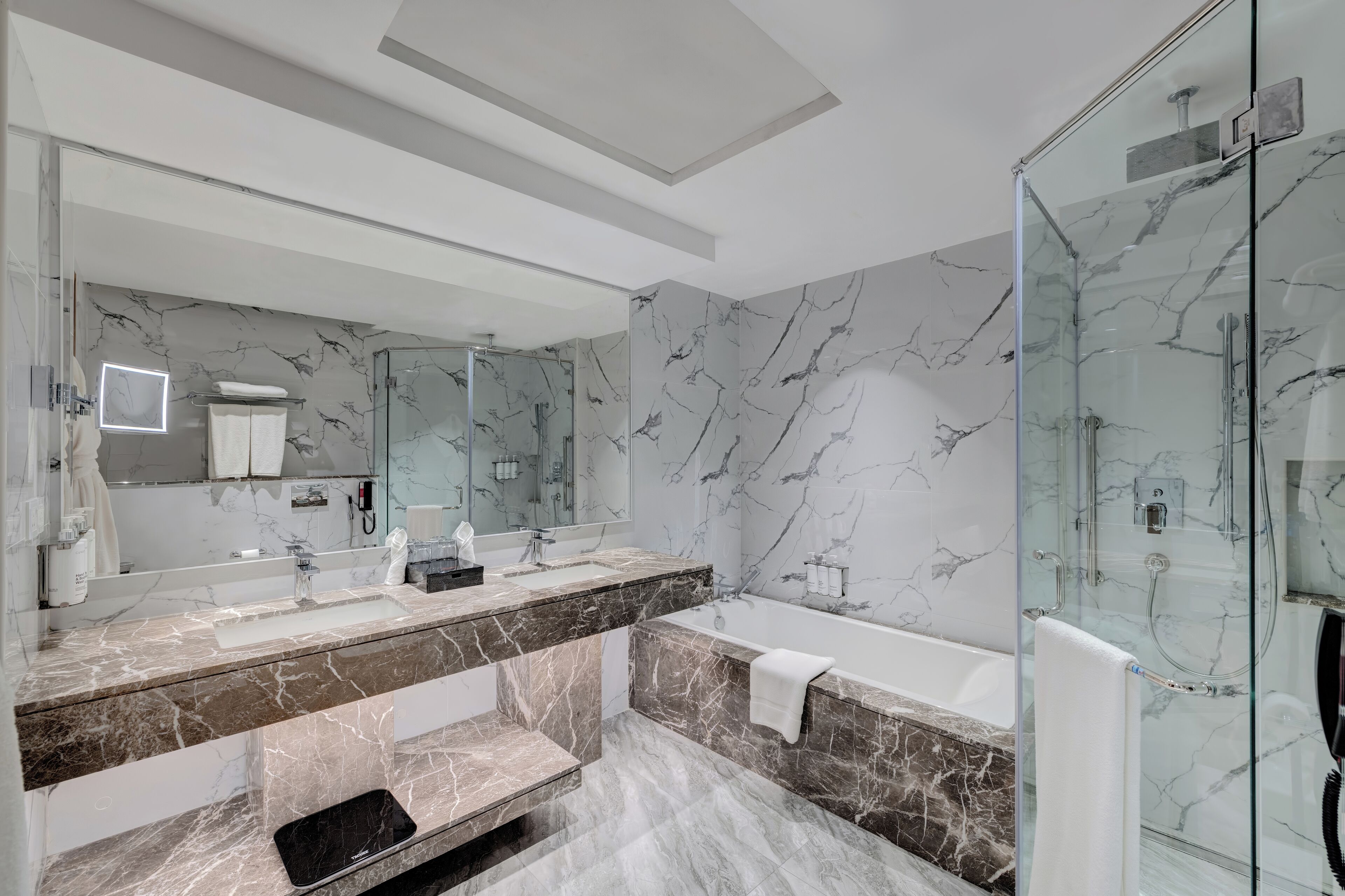 A modern bathroom with a marble vanity, a large mirror, a glass shower enclosure, and a bathtub.