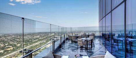 A rooftop terrace with tables and chairs, offering a panoramic city view.