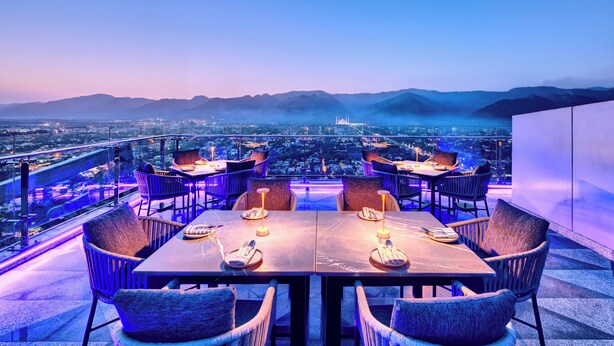 A rooftop dining area with tables and chairs, overlooking a cityscape and mountains. - Movenpick Centaurus Islamabad (Islamabad)