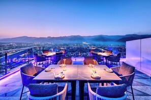 A rooftop dining area with tables and chairs, overlooking a cityscape and mountains. - Movenpick Centaurus Islamabad (Islamabad)