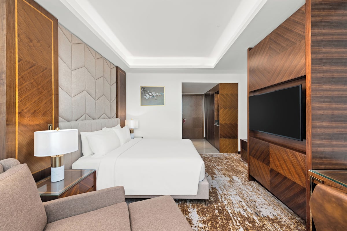 A modern hotel room with a large bed, a TV, a sofa, and a desk.
