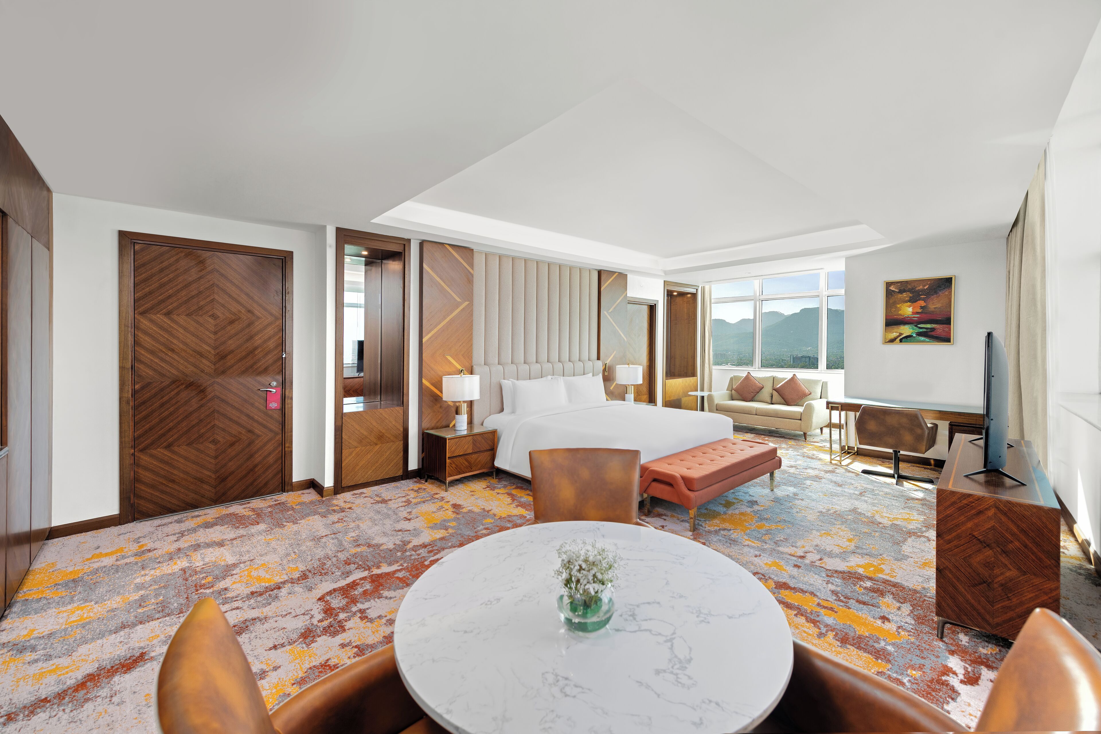A hotel room with a bed, seating area, and a view of the city.