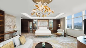 A modern hotel room with a large bed, a sofa, a coffee table, and a view of the city through large windows. - Movenpick Centaurus Islamabad (Islamabad)