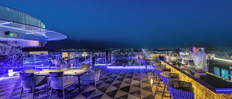 A rooftop bar with a checkered floor, bar stools, and a bartender.