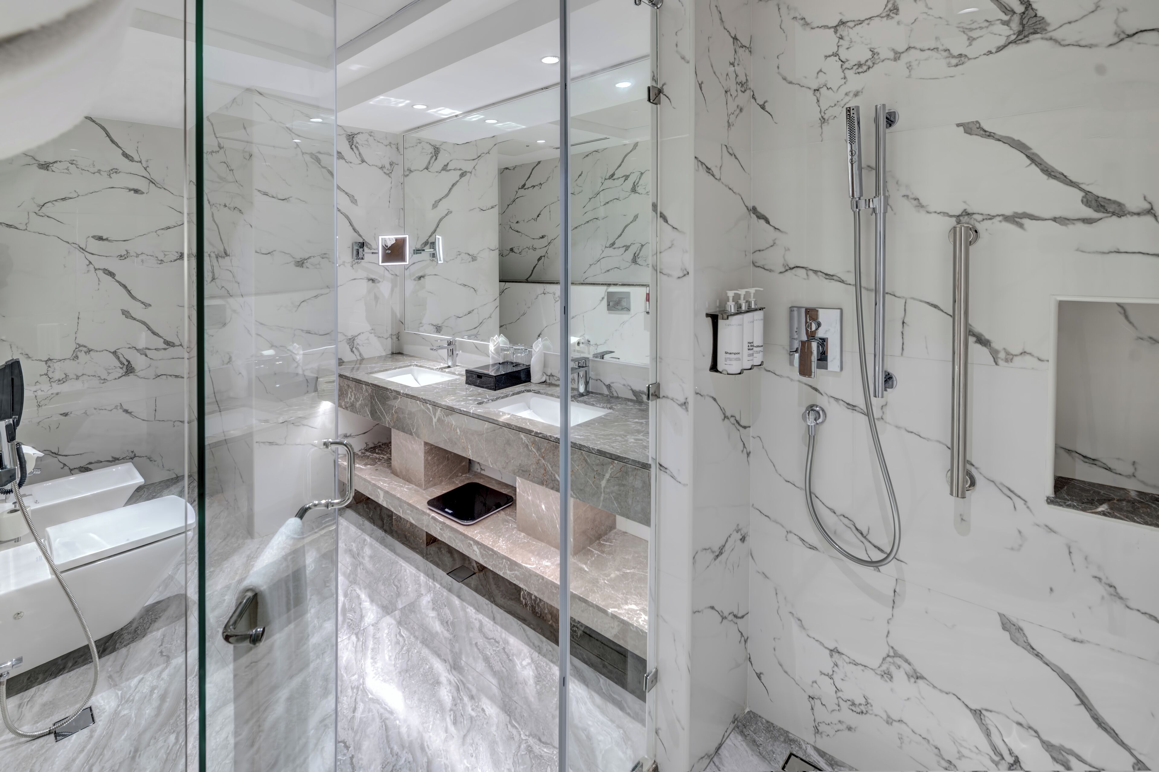 A modern bathroom with marble walls, a glass-enclosed shower, and a vanity with a sink and mirror.