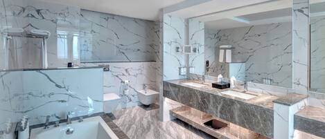 A modern bathroom with a large bathtub, a double sink vanity, and marble walls.