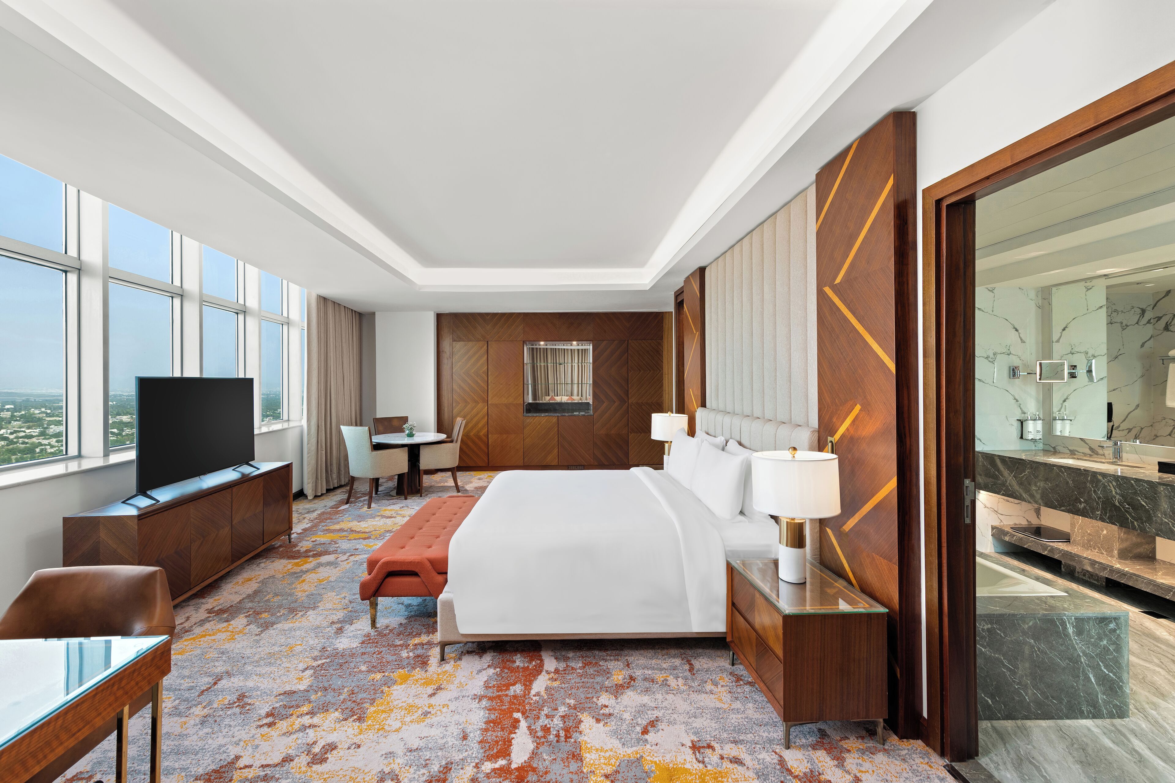 A modern hotel room with a large bed, a TV, a desk, and a view of the city.
