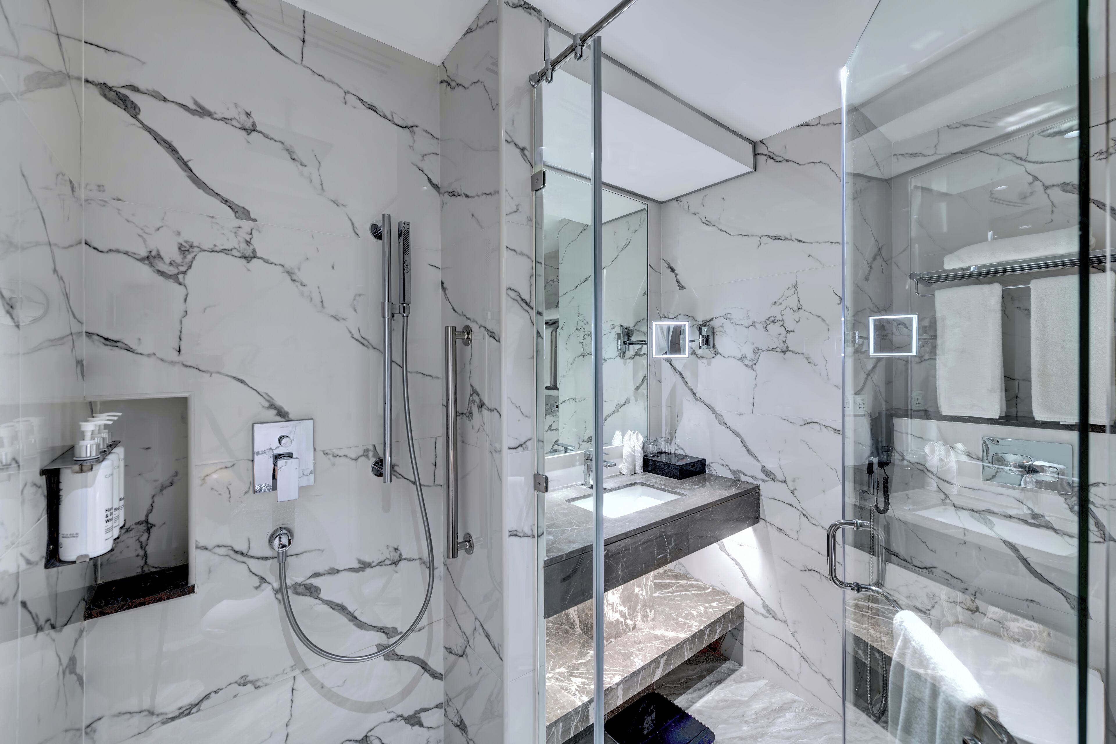 A modern bathroom with marble walls, a glass shower enclosure, and a vanity with a sink and mirror.