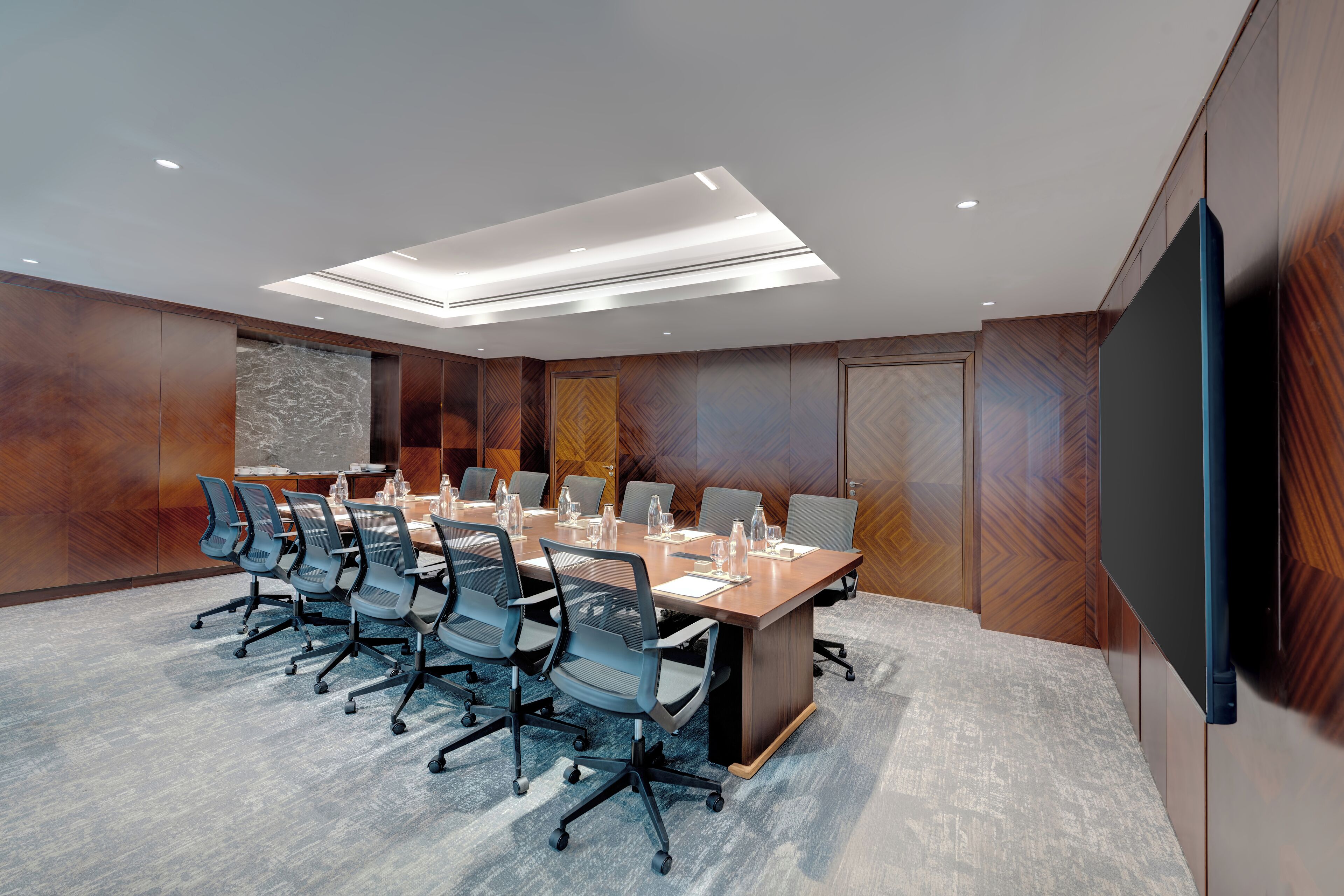 A conference room with a long table, multiple chairs, and a large screen.