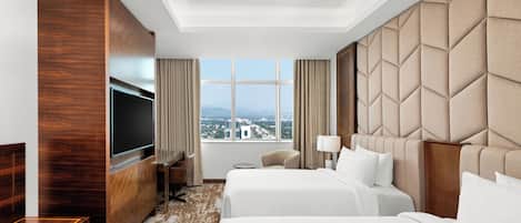 A hotel room with two beds, a TV, a desk, and a large window with a city view.