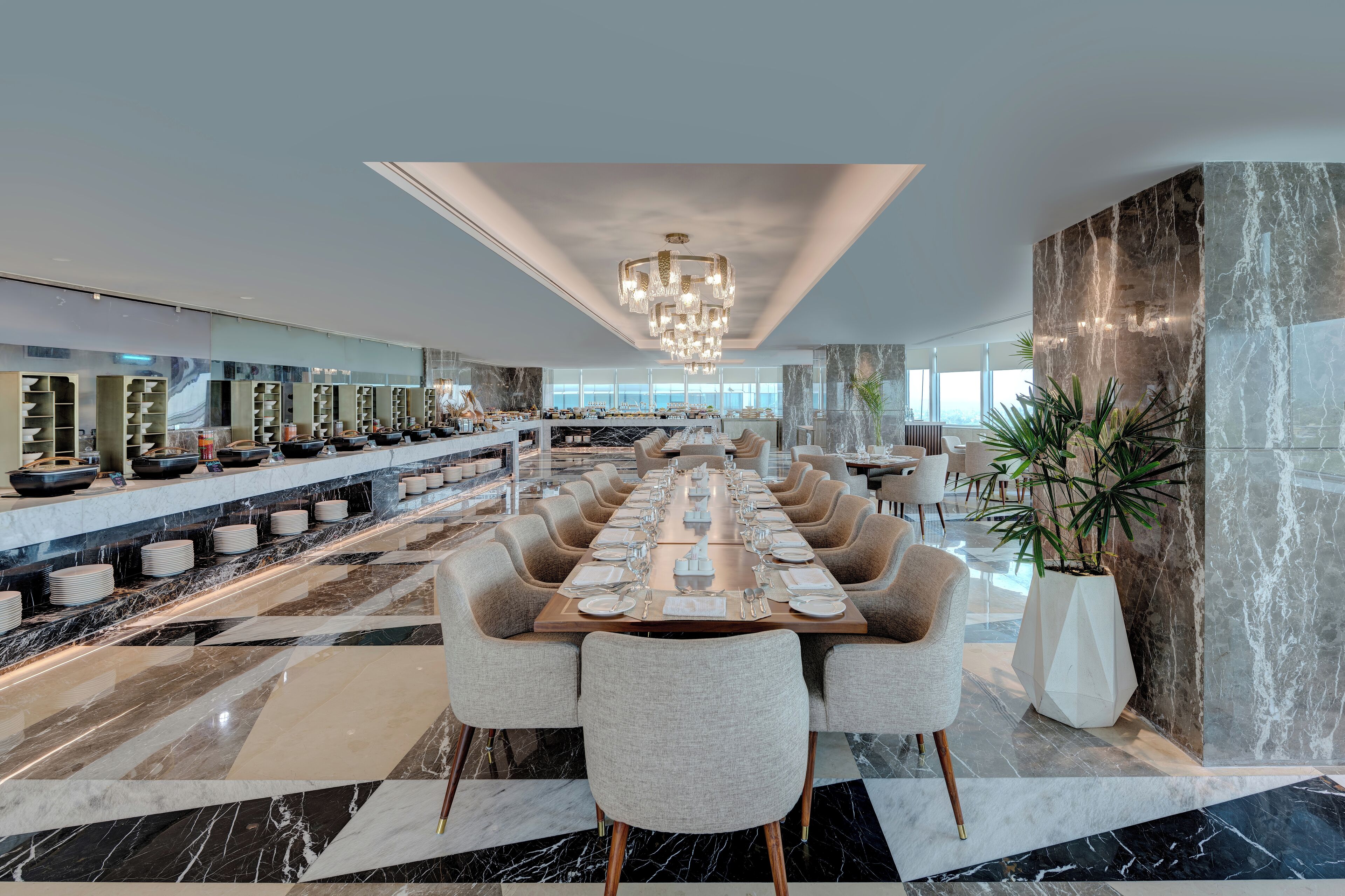 Une salle à manger spacieuse avec une longue table dressée pour accueillir de nombreux convives, entourée de chaises modernes et d’un lustre.