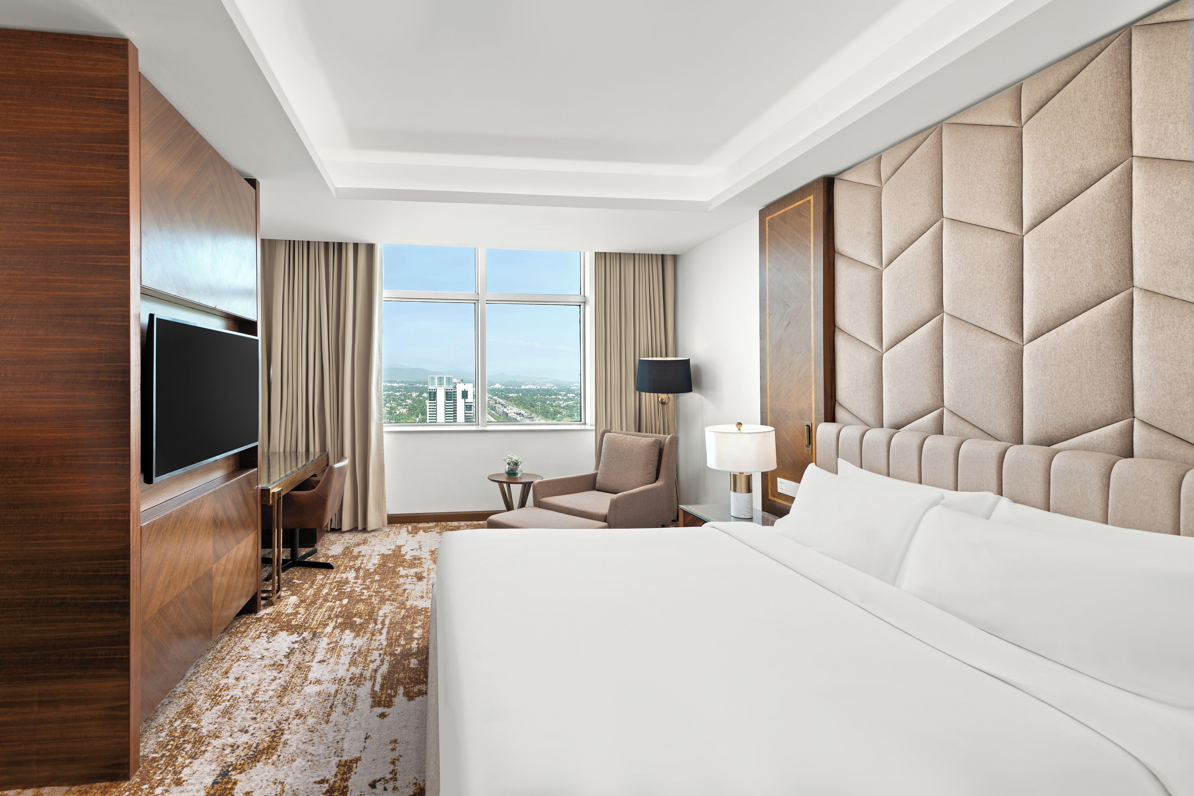 Una habitación de hotel con una cama grande, televisión, una silla, una mesita y vistas a la ciudad.