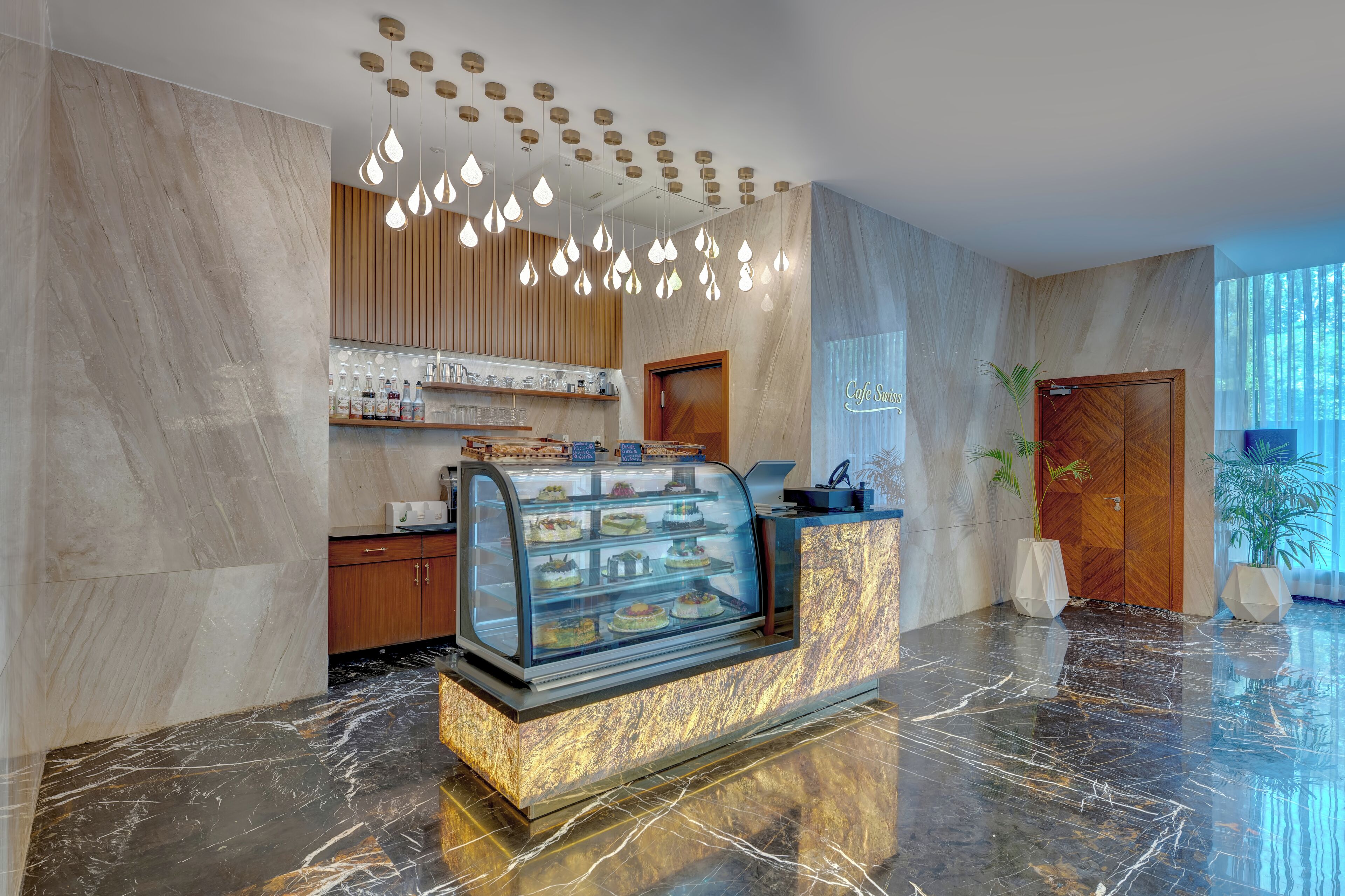 Eine moderne Hotelhalle mit einem Marmor-Rezeptionsschalter, einer Glaskuppel mit Desserts, Holzvertäfelung und einem großen Fenster mit Tageslicht.