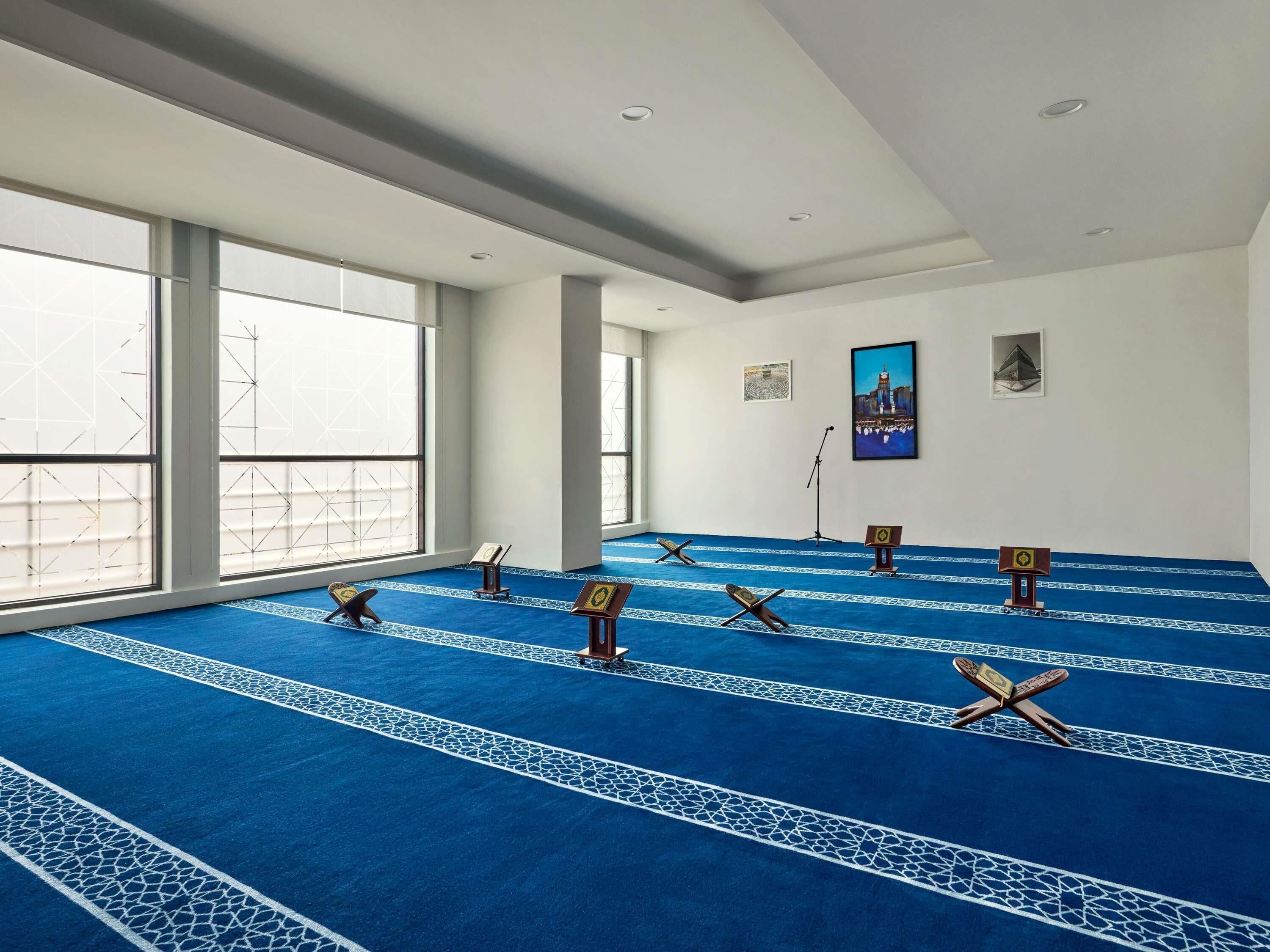 A prayer hall with a blue carpet, prayer mats, and a microphone stand.