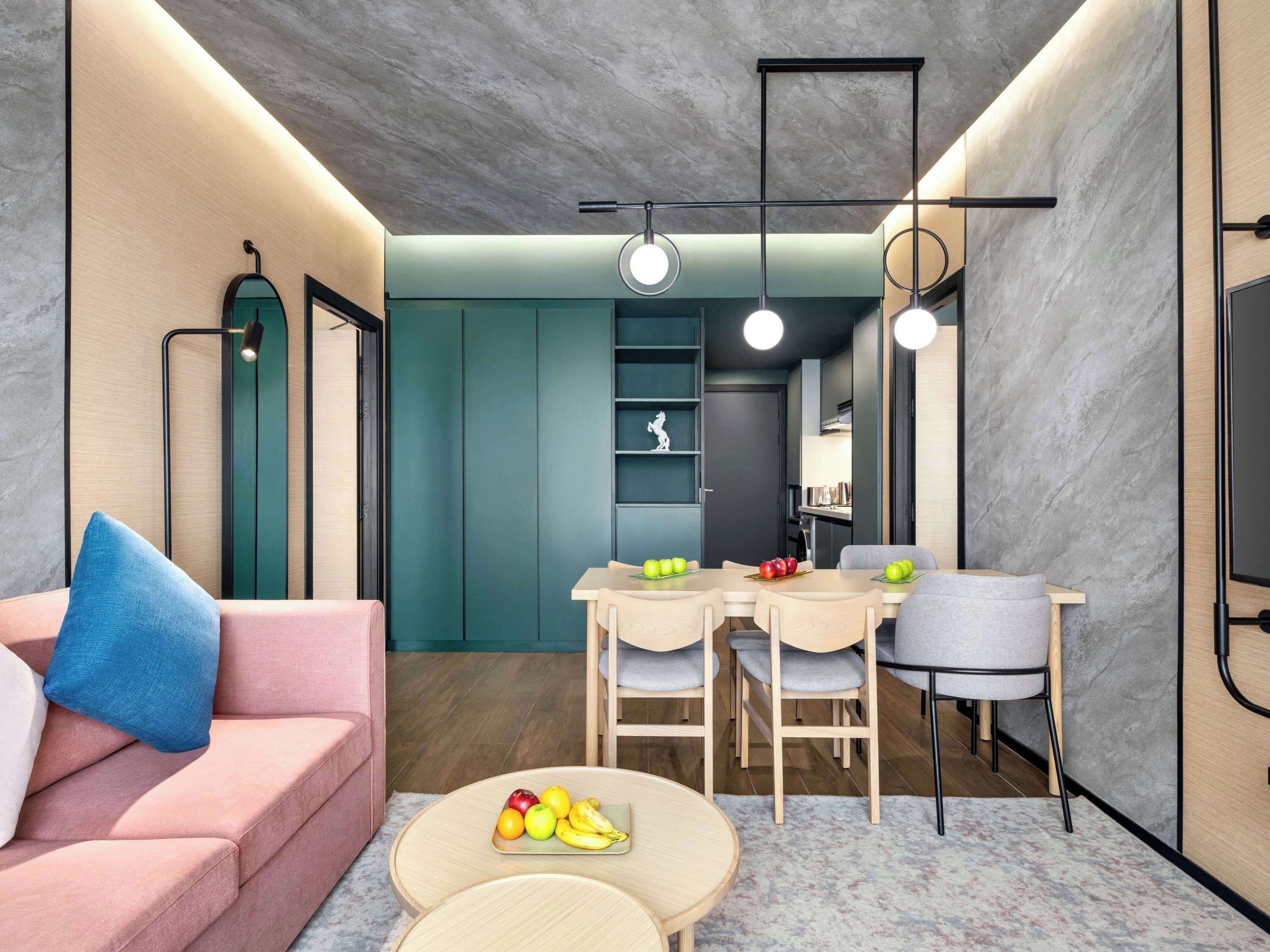 Een moderne woonkamer met een roze bank, een ronde salontafel met fruit, en een eethoek met een tafel en stoelen.