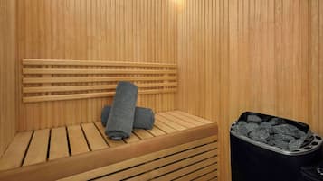 A wooden sauna with a bench, a towel, and a charcoal container.