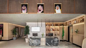 A modern hotel lobby with a reception desk, potted plants, a TV screen, and framed portraits on the wall. - Novotel Residences Makkah (Makkah)