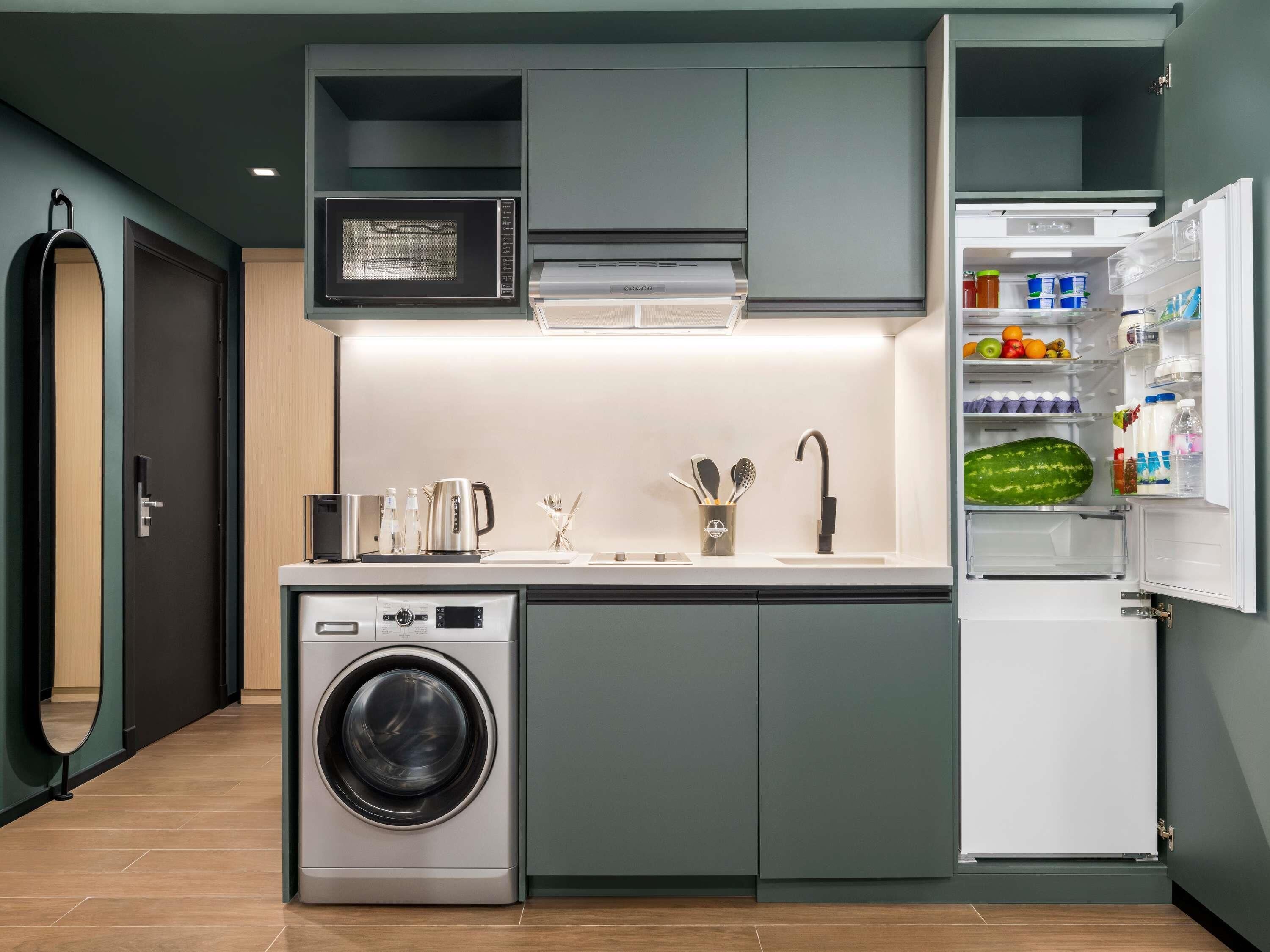 Cocina compacta con lavadora, microondas y refrigerador, además de una puerta con toallero.