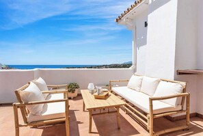 Ein Balkon mit einer weißen Couch, zwei Stühlen, einem kleinen Tisch und einem Blumentopf.