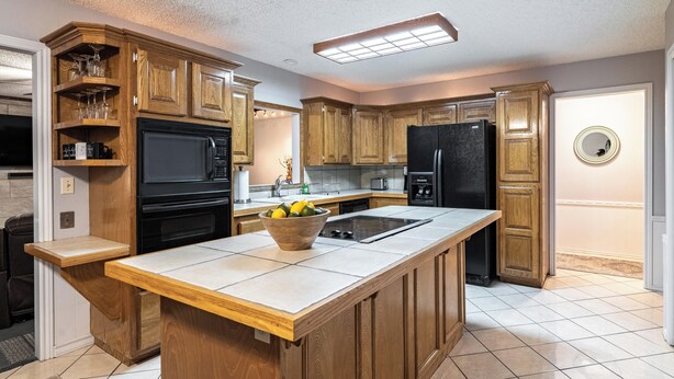 A kitchen with wooden cabinets, a black refrigerator, a microwave, and a large island with a bowl of fruit.