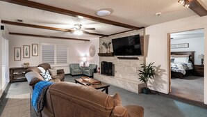 A living room with a brown leather sofa, a patterned armchair, a coffee table, and a television mounted on a stone wall.