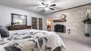 A bedroom with a bed, a ceiling fan, a fireplace, and a large mirror.
