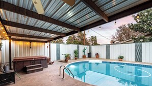 A covered outdoor swimming pool with a wooden deck, a barbecue area, and potted plants.